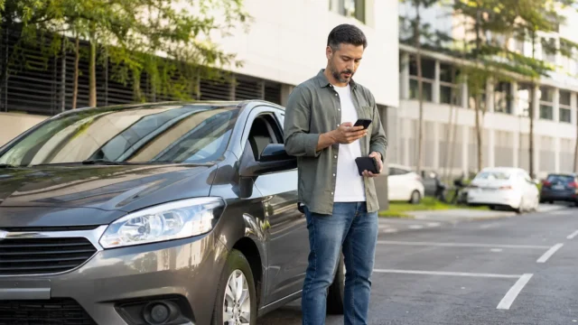 Motorista consulta o celular ao lado de um carro antes de renovar a CNH